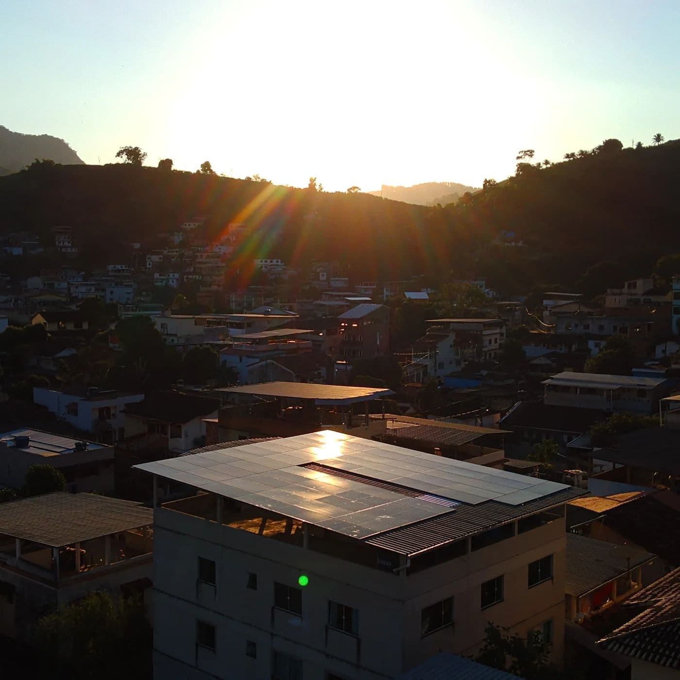 Painéis solares na laje de um edifício ao pôr do sol, com a cidade ao fundo